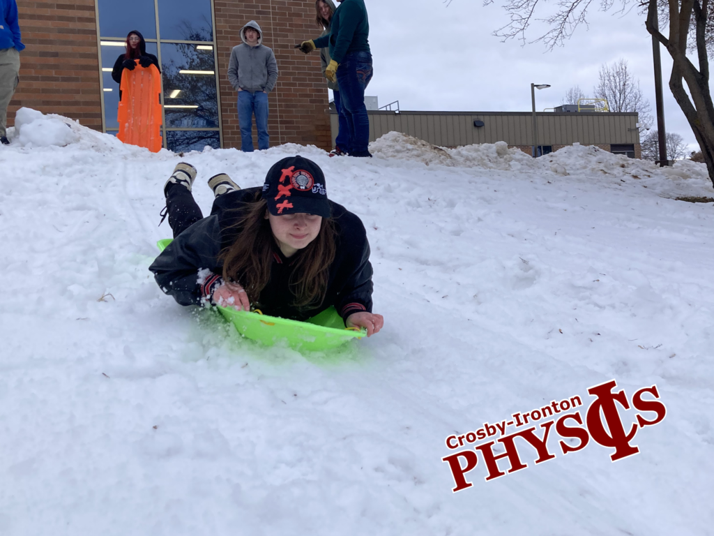 female student sledding down a hill on her stomach from Physics class