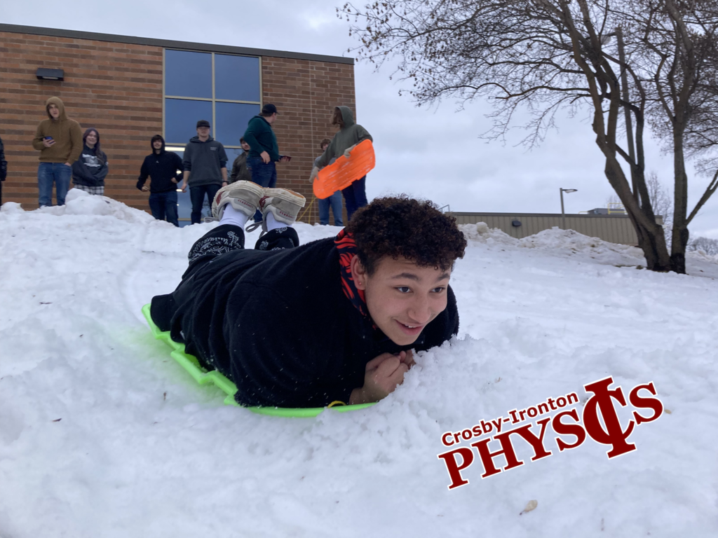 Male student laying on his stomach sledding down a hill in physics class