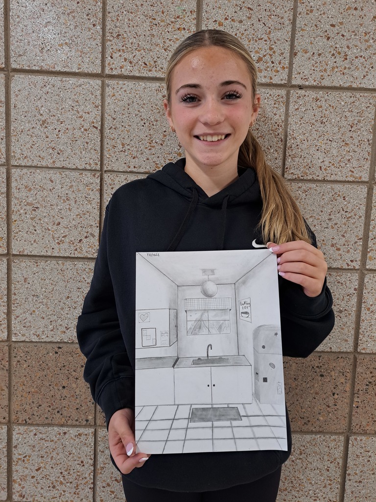 female student holding a 1 point perspecitive pencil drawing of a kitchen setting