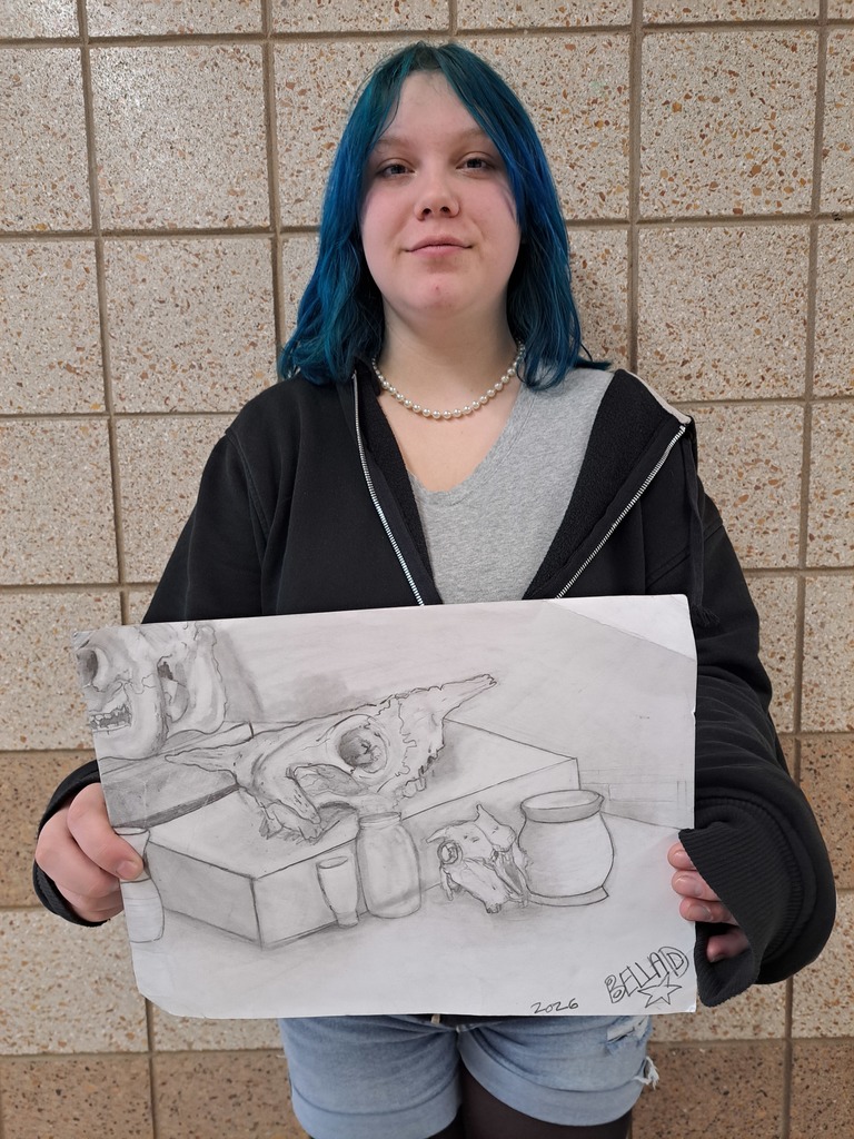female student showing off her still life drawing  of a skull on top of a box and some small vases