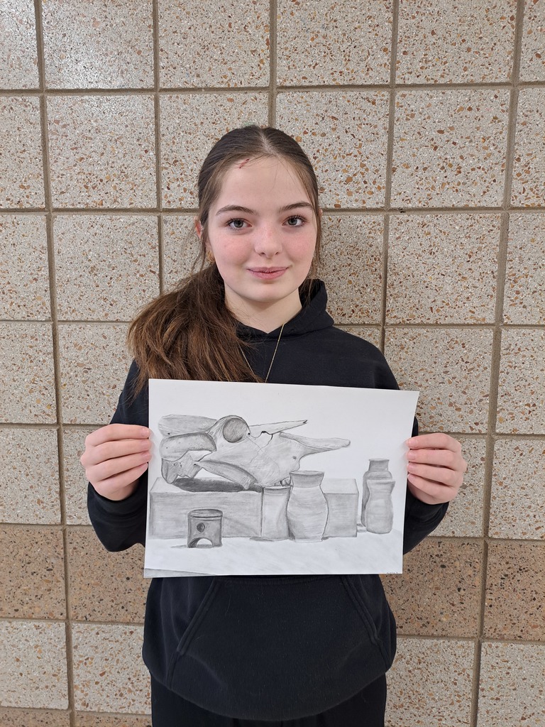 female student holding a still life pencil drawing of a skull with small vases surrounding it