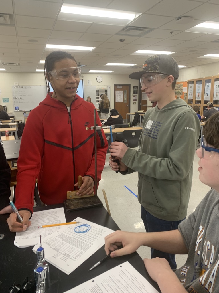 male students adding weights to rubberbands and measuring the stretch