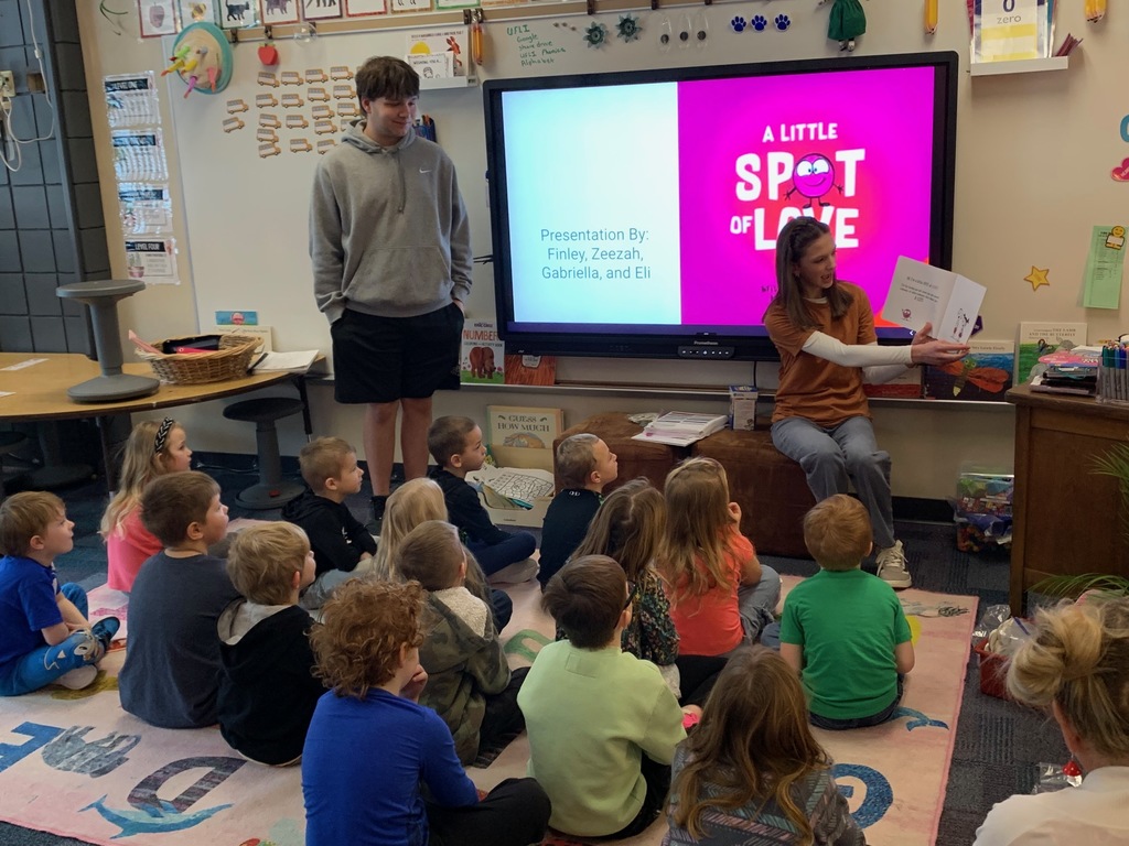 male and a female HS student in front of a classroom of kindergarteners reading a book about emotions