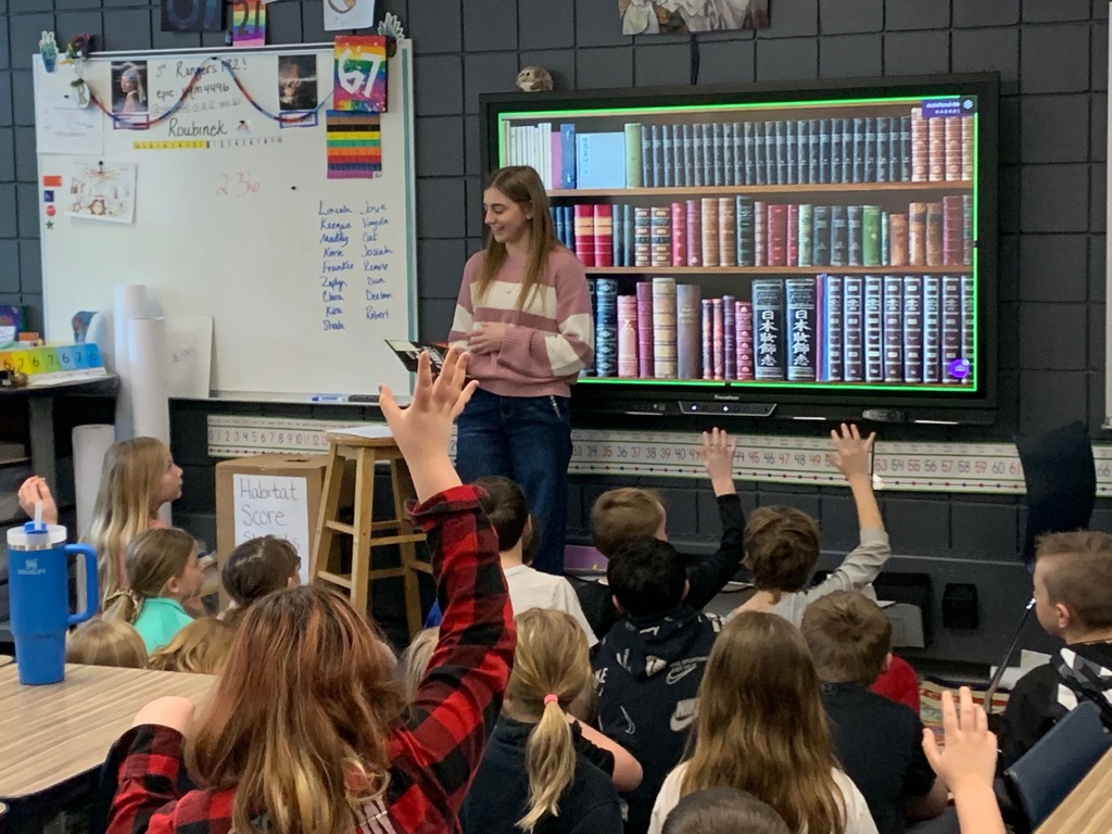 Female HS student standing in front of a class with students raising their hands