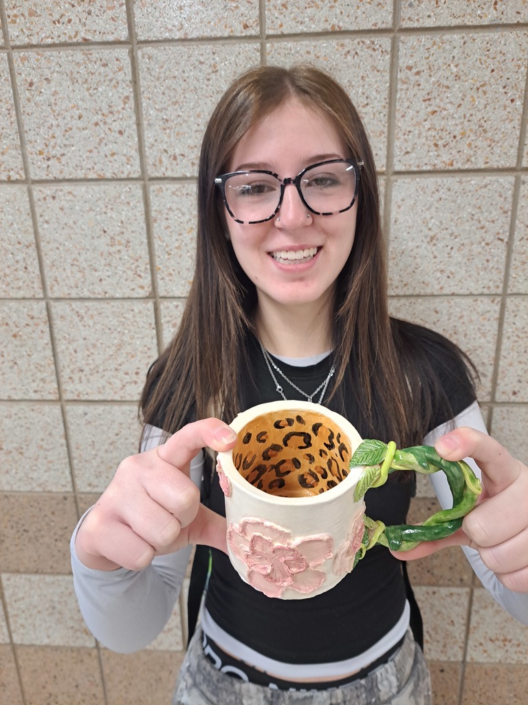female student holding her clay mug with a flower on the outside, a vine handle and leopard print on the inside
