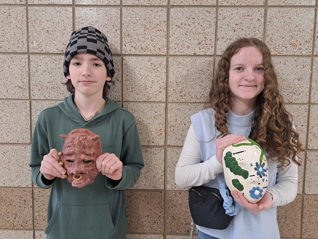 two 9th grade students holding 3d clay masks that they made in art class