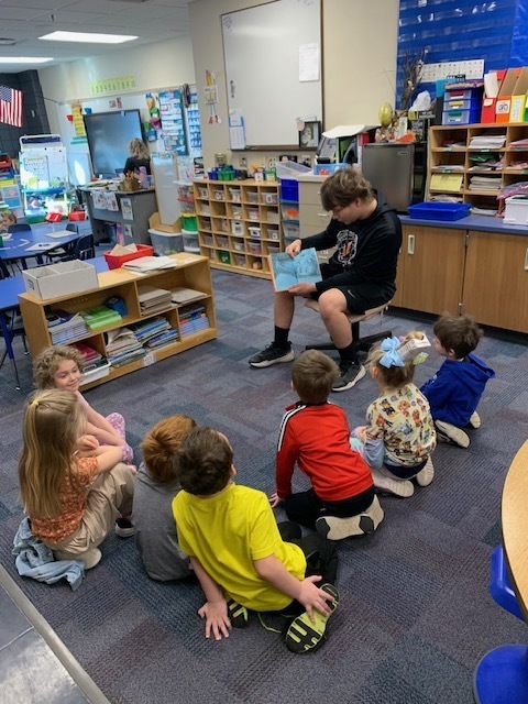 high school male student reading to CRES students a dr. seuss book 