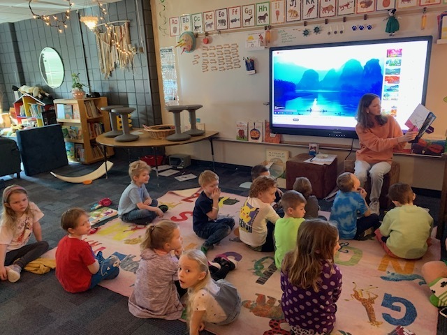 students sitting on the floow listing to a children's lit student read a book 