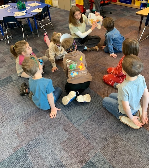 Student in Children's lit class sitting on the floor with CRES students reading a book 