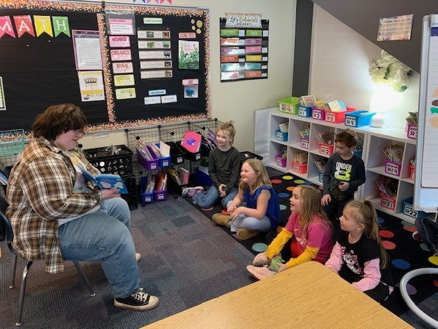 a few CRES students listening to a dr. seuss book being read to them by a high school student
