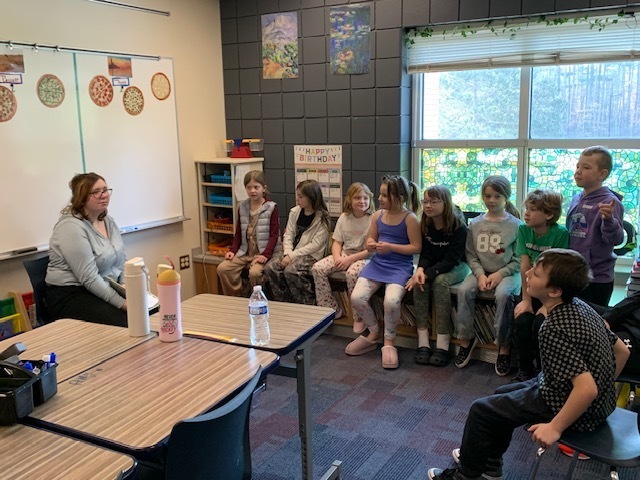 students sitting in the windw sill listening to a book being read to them by a high school student