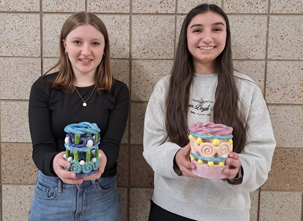 two female 9th graders holding their coil pot creations from art class