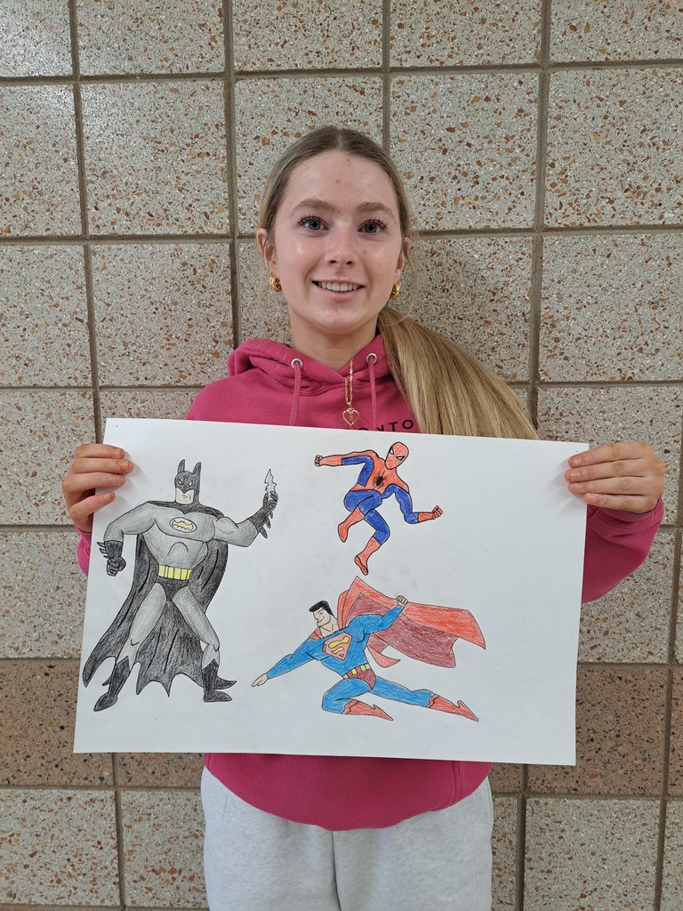 female student holding pencil drawings of superman, batman and spiderman