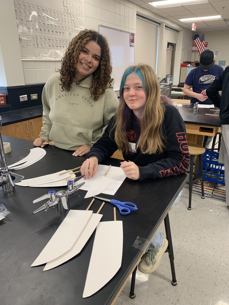 two females sitting at a table with their wind turbine papers on a stick