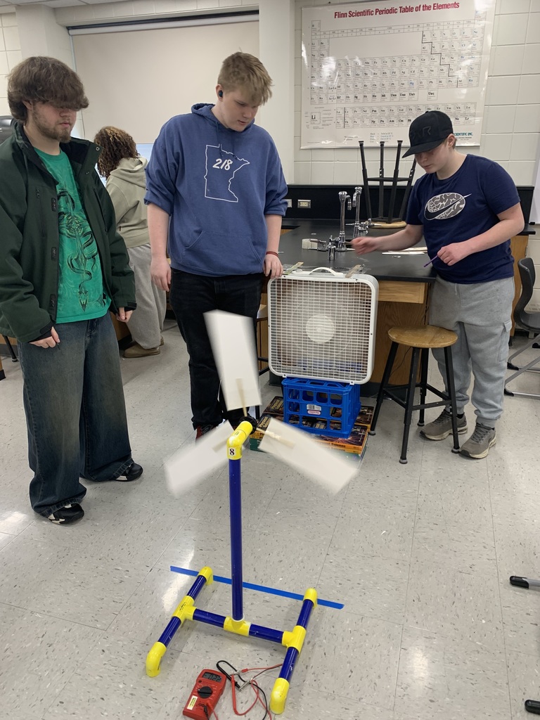 three male students using a fan to blow their wind turbine that they made
