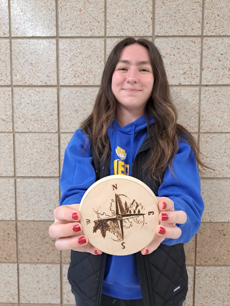 female student holding a circular compass out of wood that she wood burned