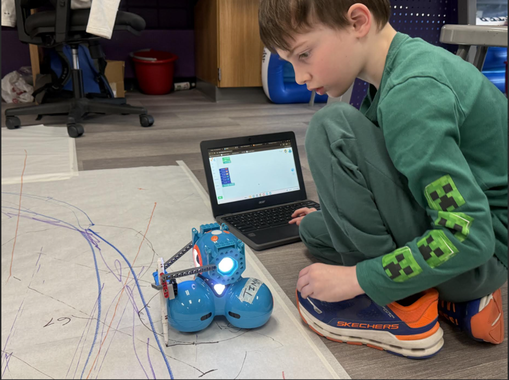 male 2nd grader working on his computer to code is robot