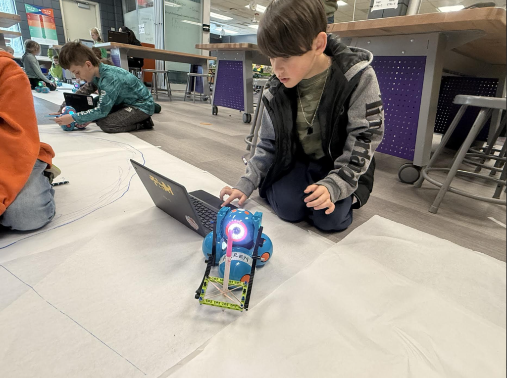 male 2nd grader coding his robot to draw with the marker it is holding
