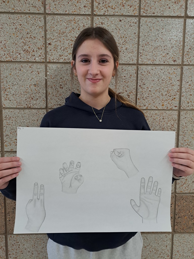 female student holding a large piece of paper with 4 drawings of hands doing different things: peace sign, fist, showing the palm.