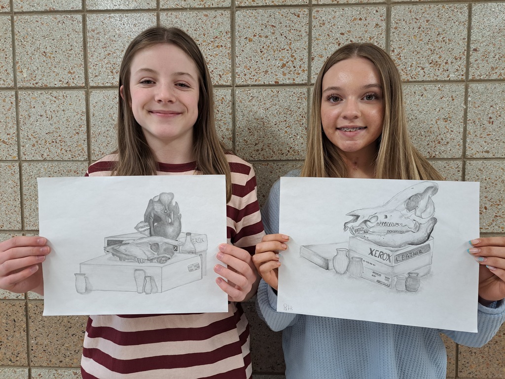 Two 8th grade females holding still life drawings