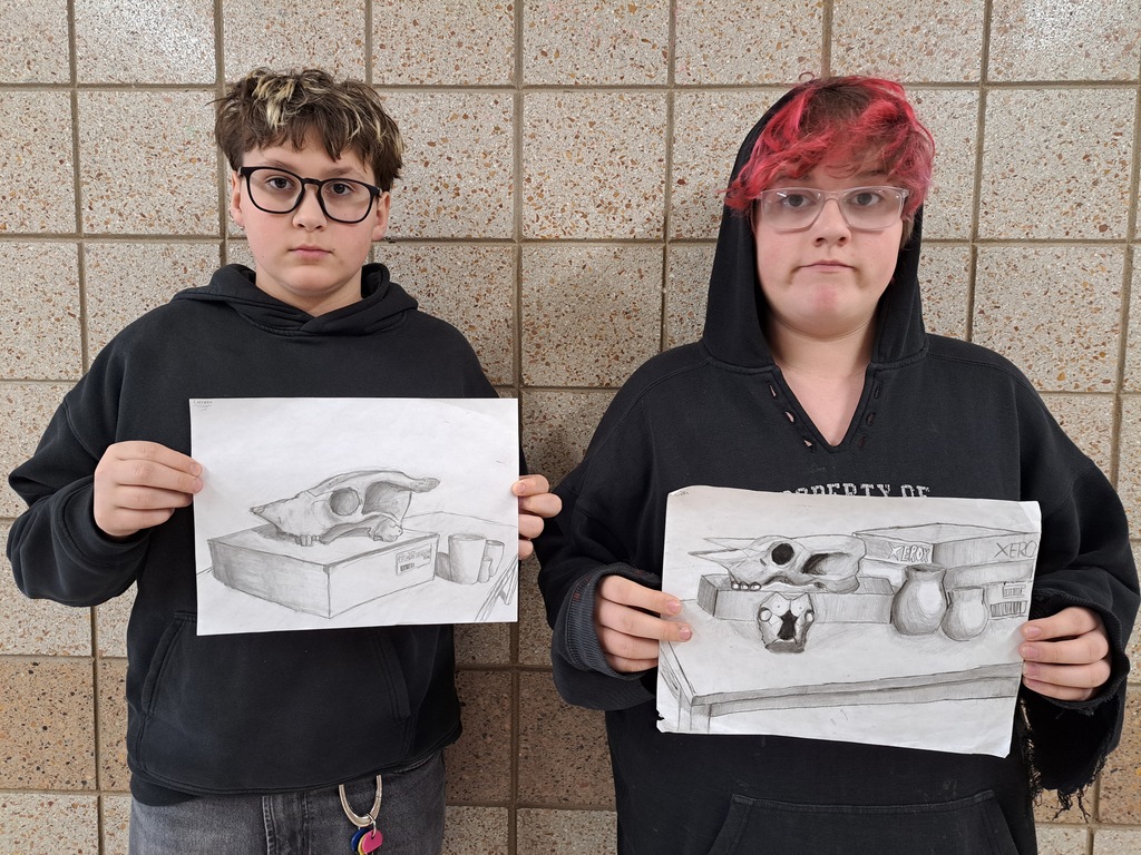 Two students holding still life observation drawings