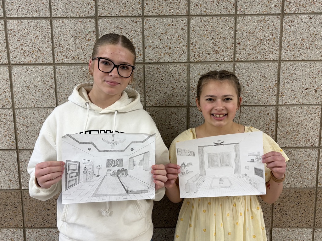 two females holding 1 point perspective drawings one of bedroom the other a living room