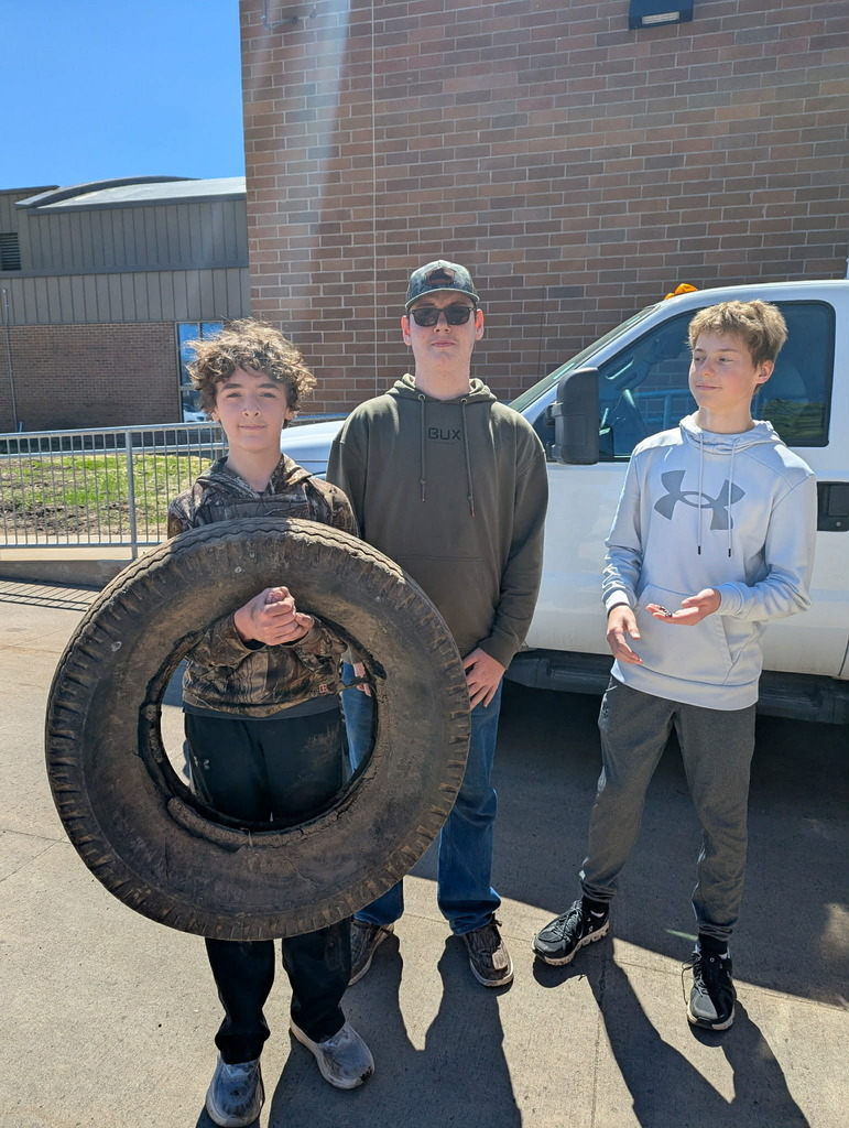 three students, one holding a tire that they collected while picking up trash