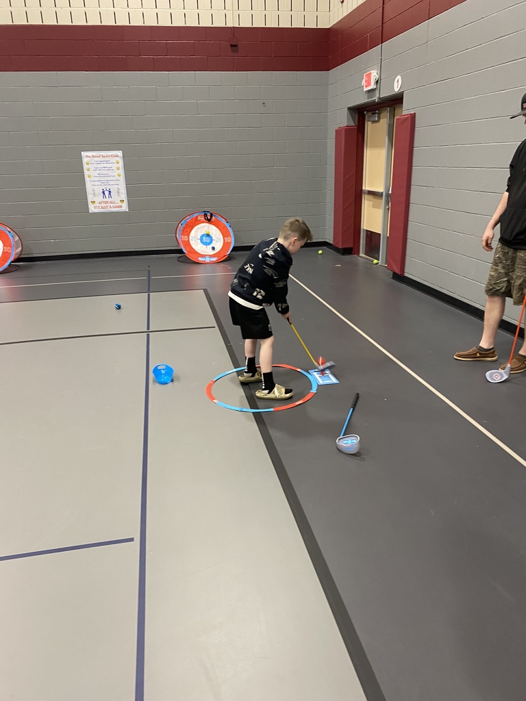 1st grade male standing in a circle in the gym putting a golf ball at his expo