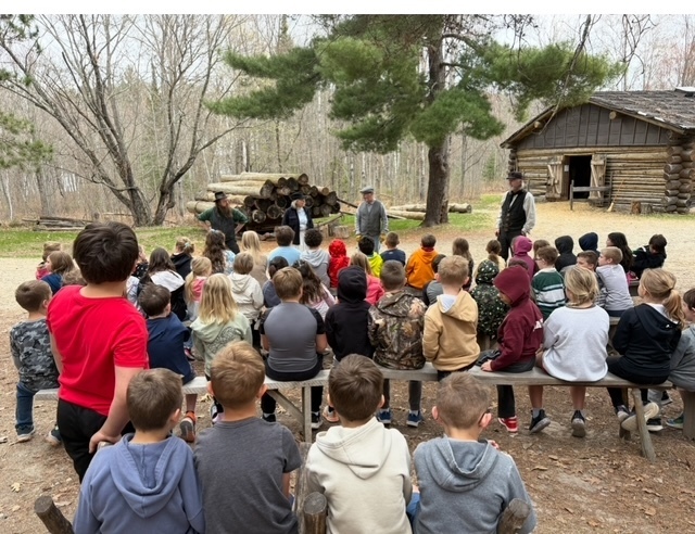 students sitting on benches listening to speakers at the forest history center on their 2nd grade field trip