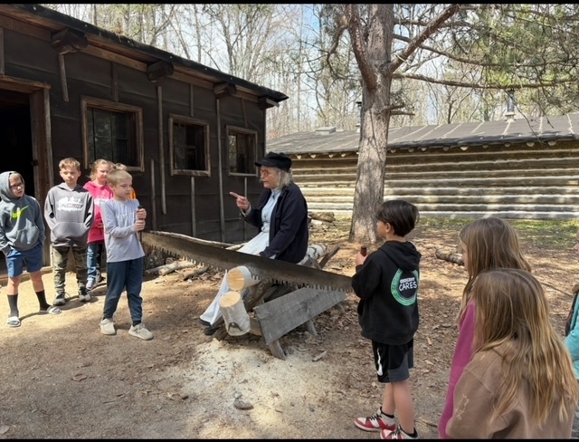 2nd gradter listening to a person speak at the forest history center while sawing