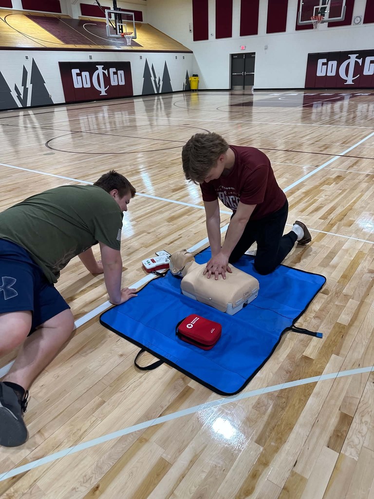 two males one watching the other performing CPR on a manaquin