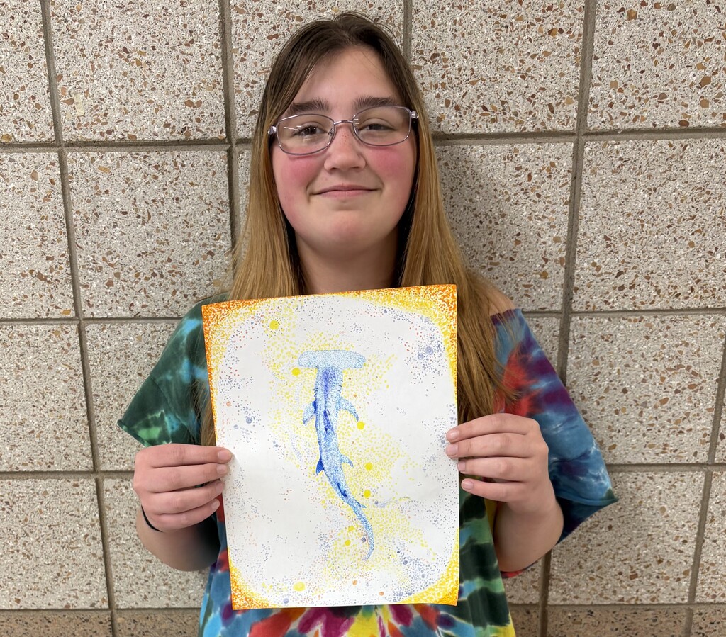 female student holding a pointellism project of a hammer head shark