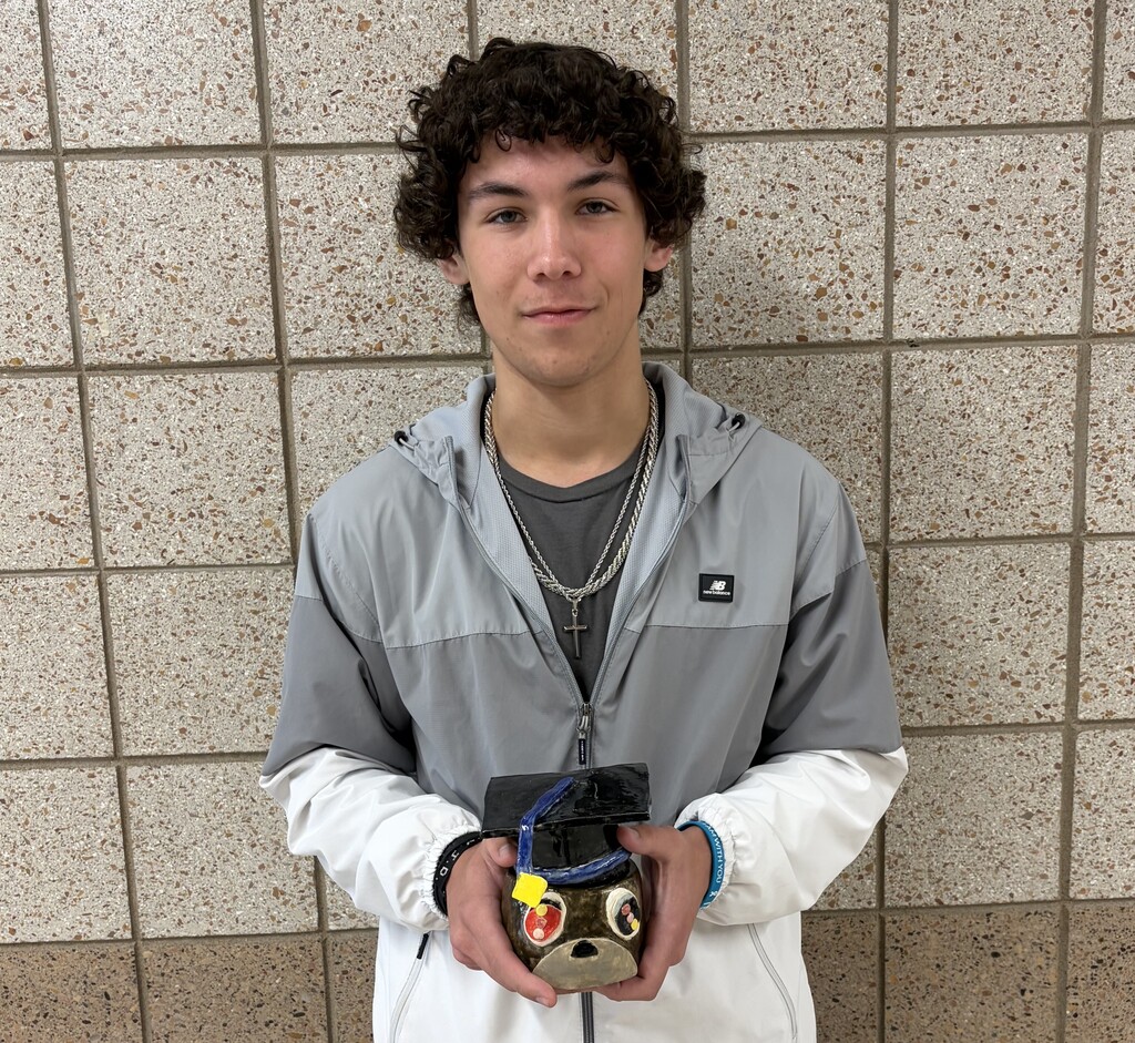 male student holding his handbuilt creature container with a grad cap