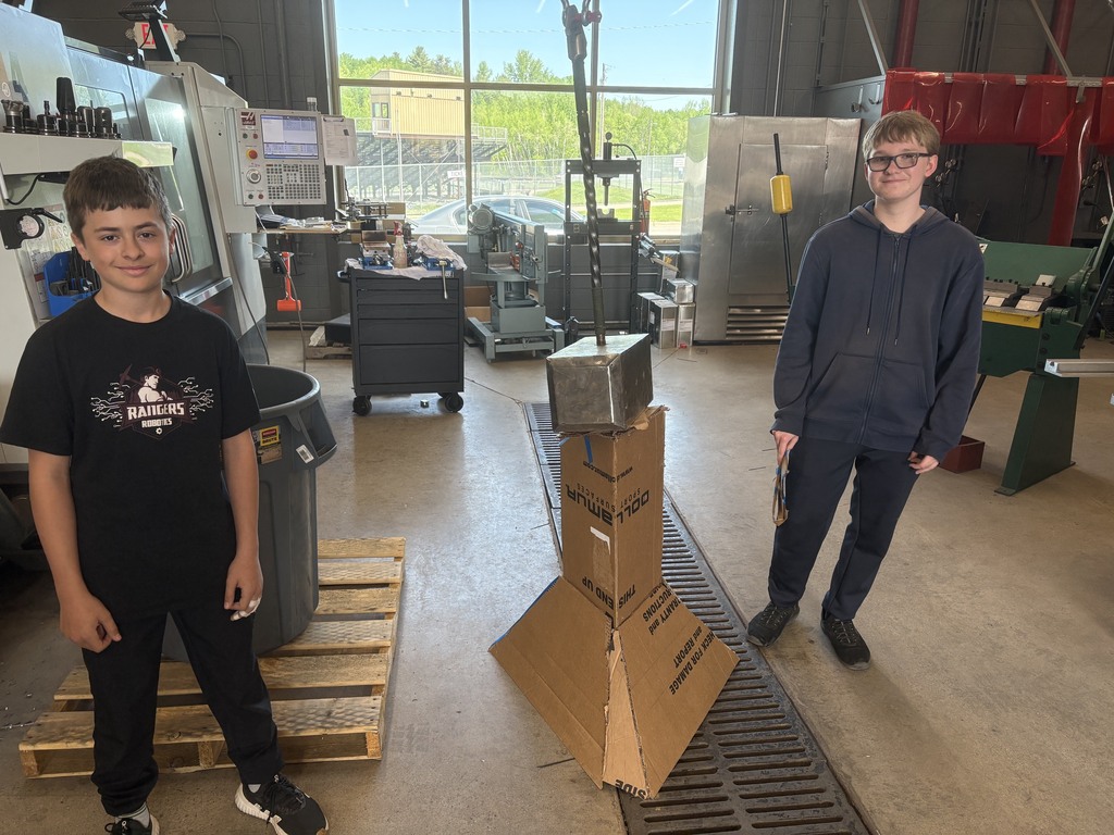 two male students standing next to their carboard design that can hold a construction hammer