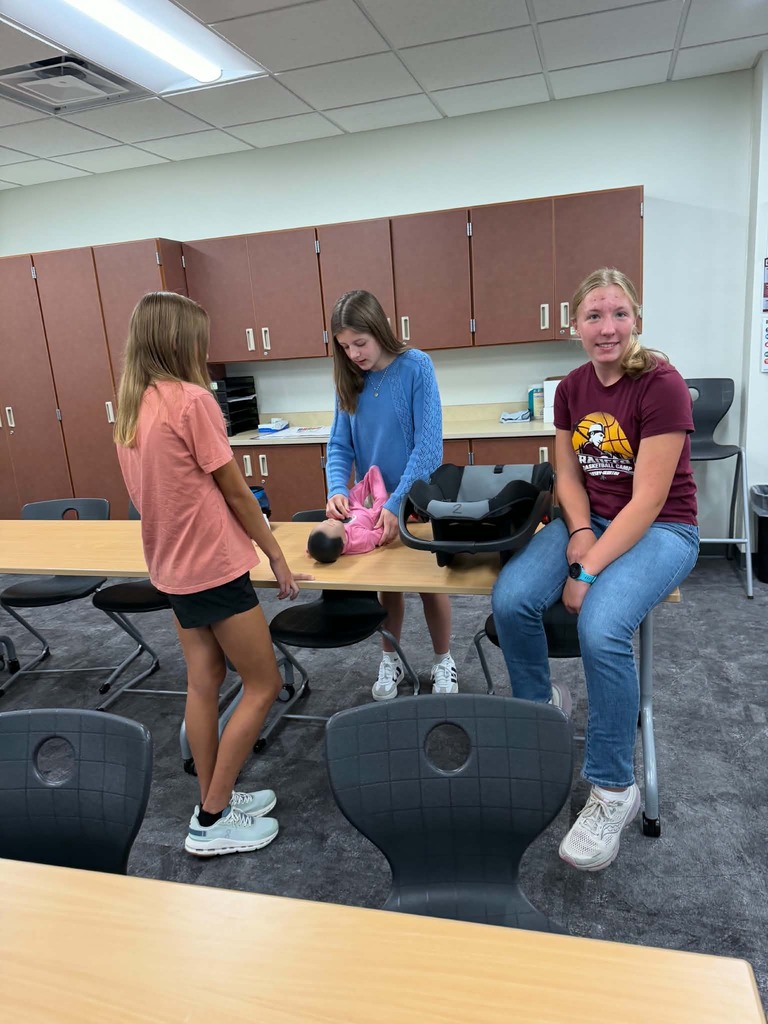three female students at a table, one of them is getting a baby dressed