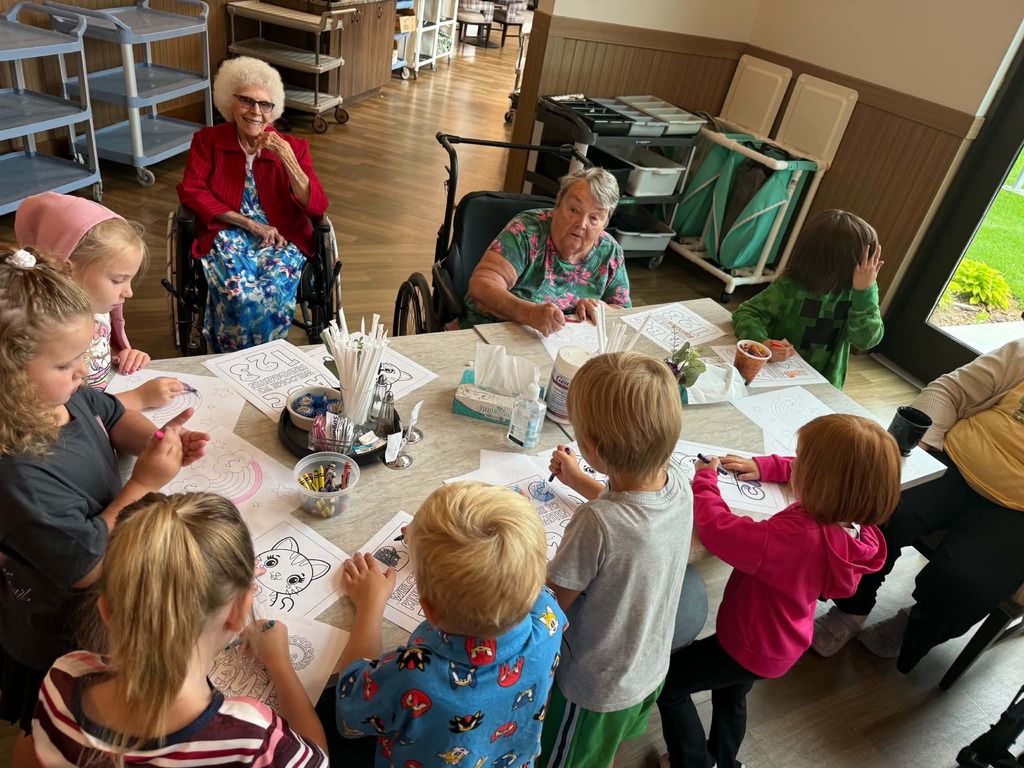 kindergartners coloring with residents at a table 