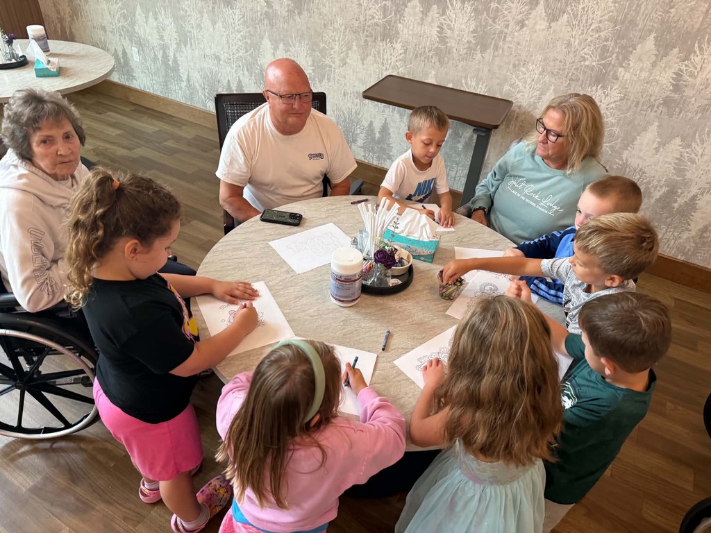 a group of kindergartners working at table with some residents