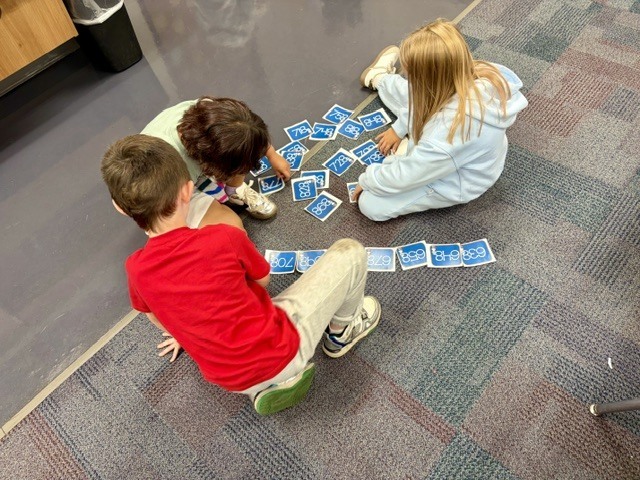 three 2nd graders sitting on the floor sorting through numbers