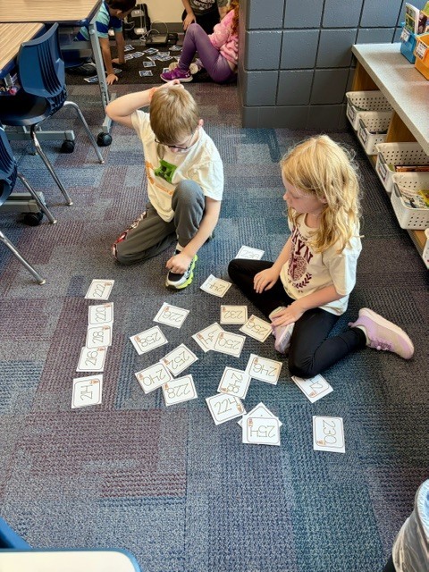 two 2nd graders sitting on the floor sorting numbers