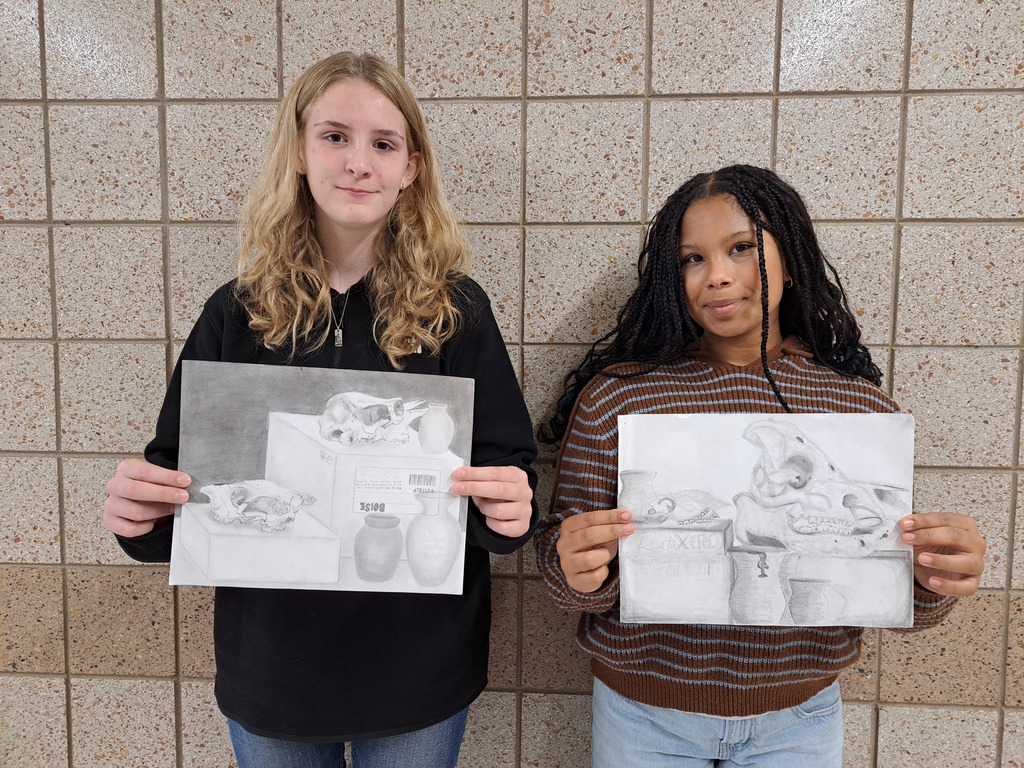 two female students with pencil drawings of an animal skull and pottery