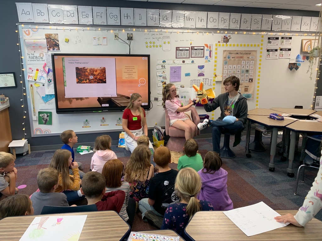 three HS students, one reading a book the other holding a puppet and the other waiting for their turn, reading to students at CRES