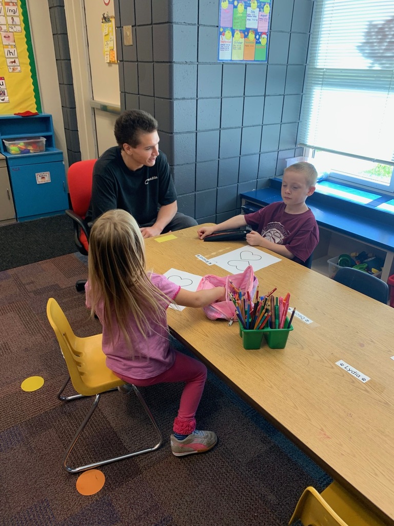 two kindergarten students sitting at a table with a HS student