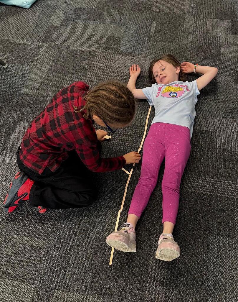 student measuring another student laying on the floor