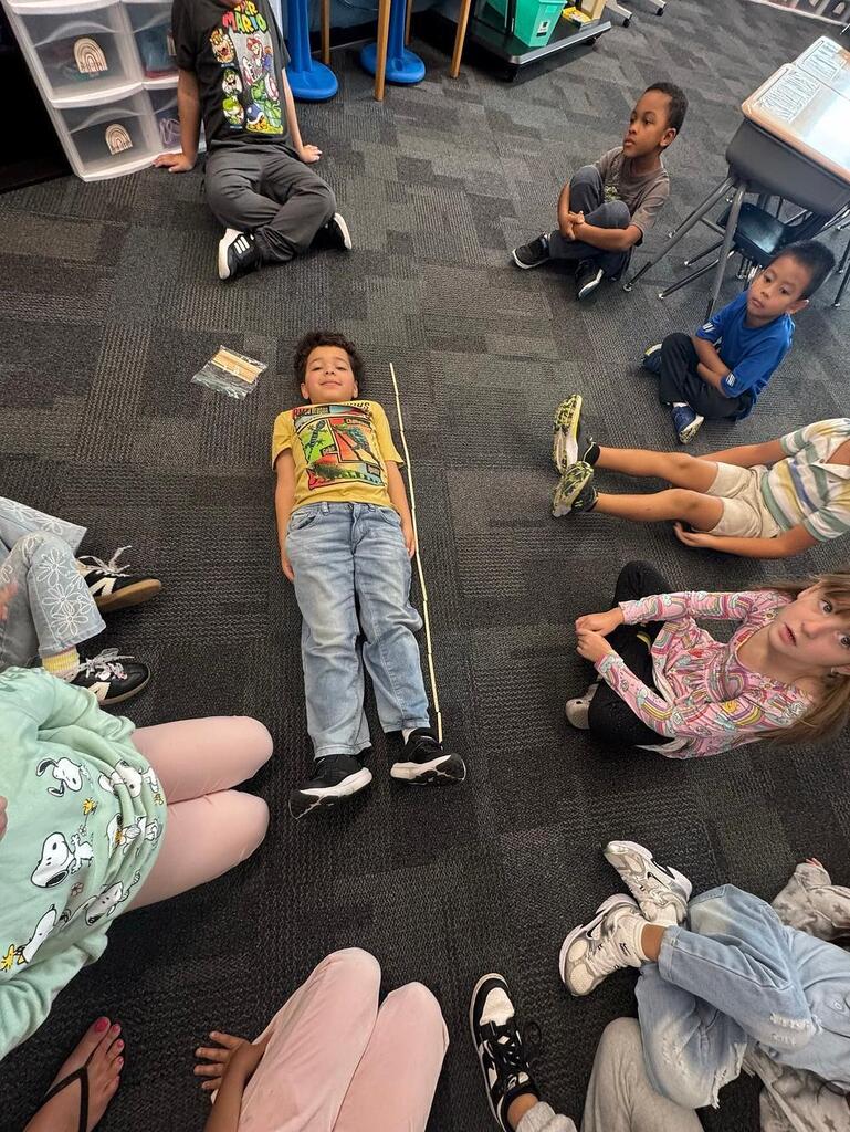 student measuring another student laying on the floor