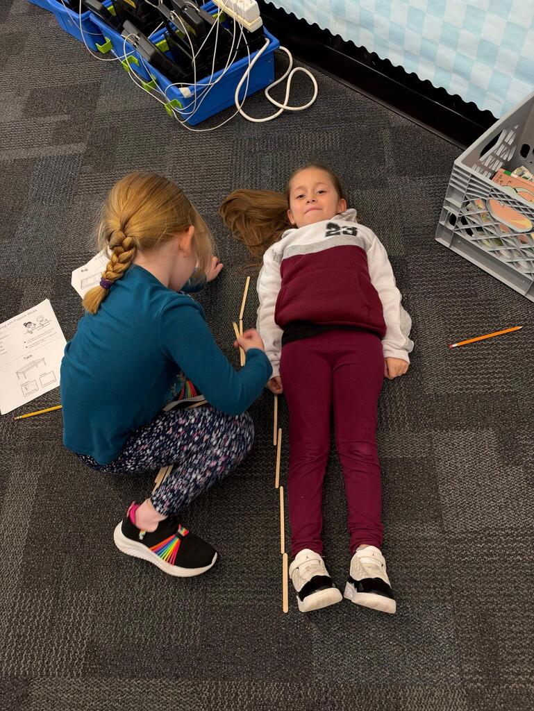 student measuring another student laying on the floor