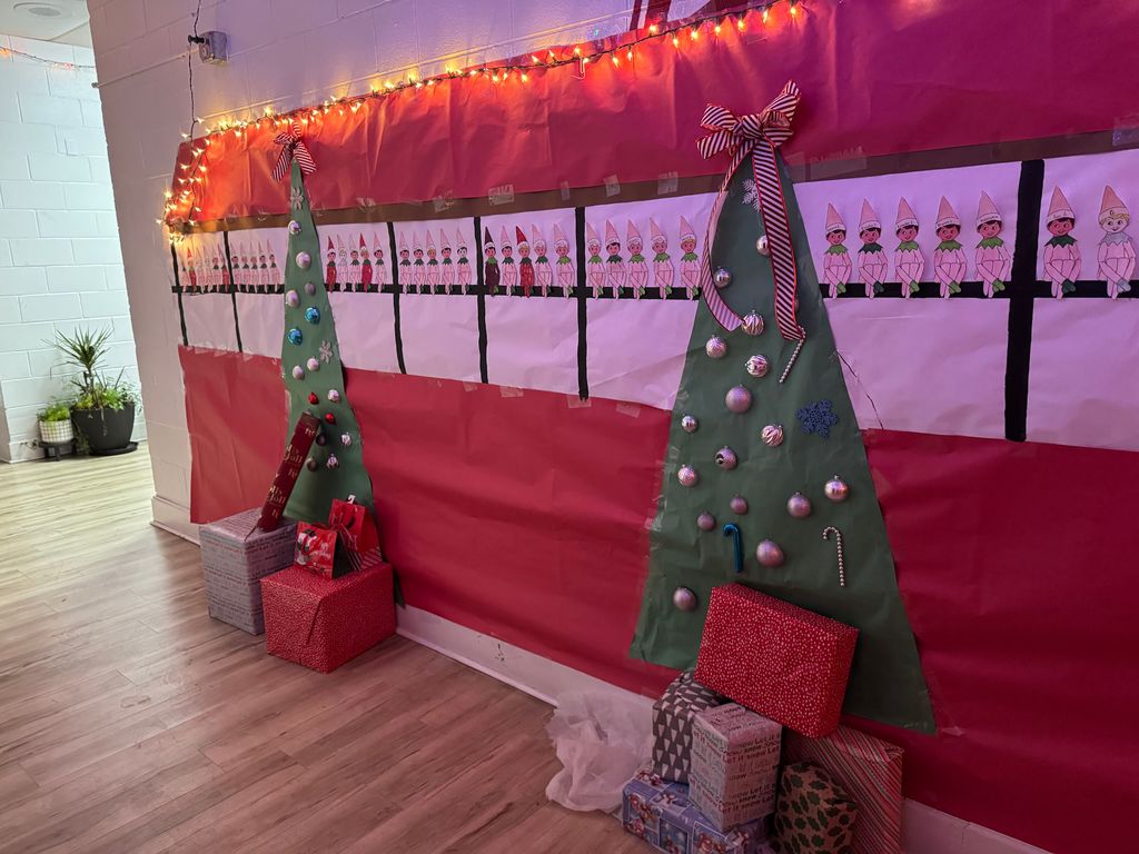 Hall with 2 paper Christmas trees with gifts beneath and a row of elves (one for each Senior)