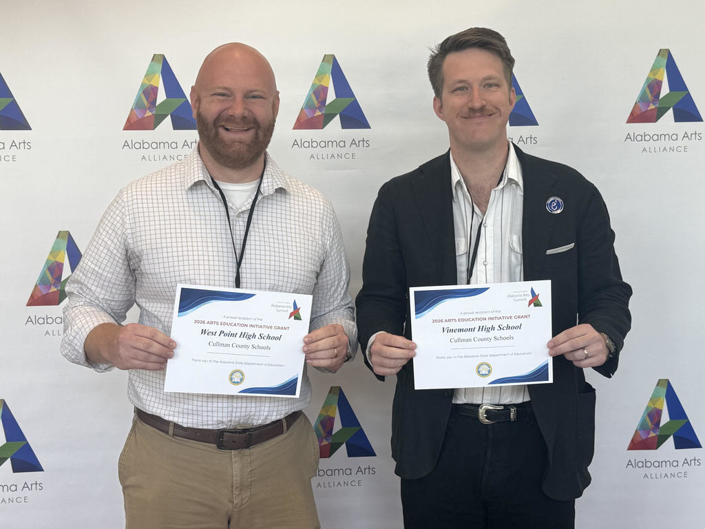 Two men holding certificates with white text and blue borders, standing before a backdrop with abstract triangular patterns.