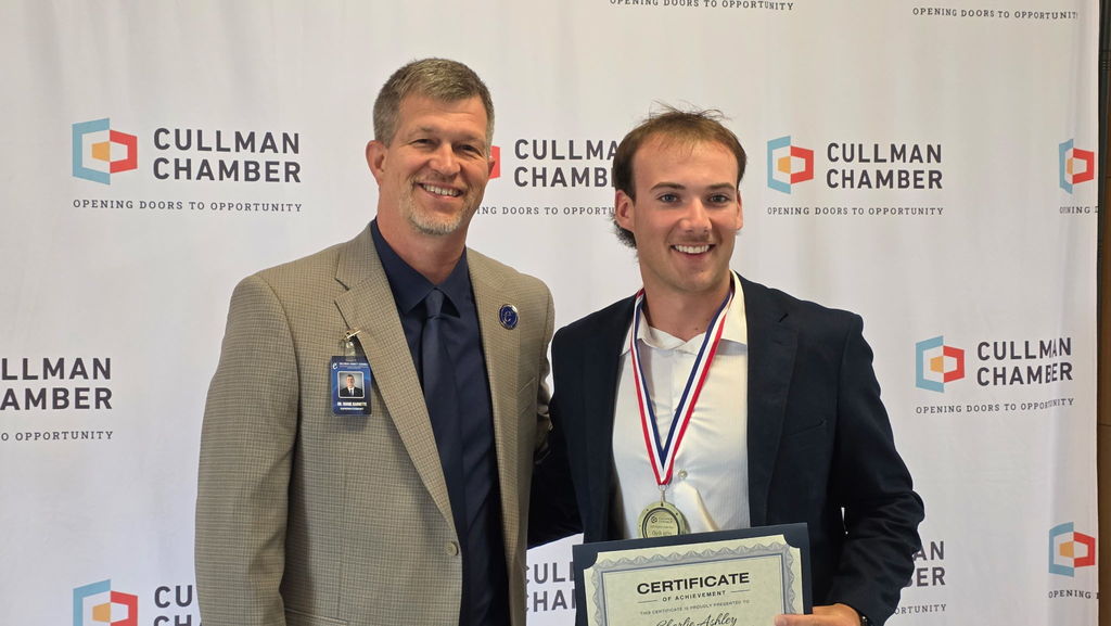 Two men stand smiling, one holding an award, against a backdrop with "Cullman Chamber" logos.