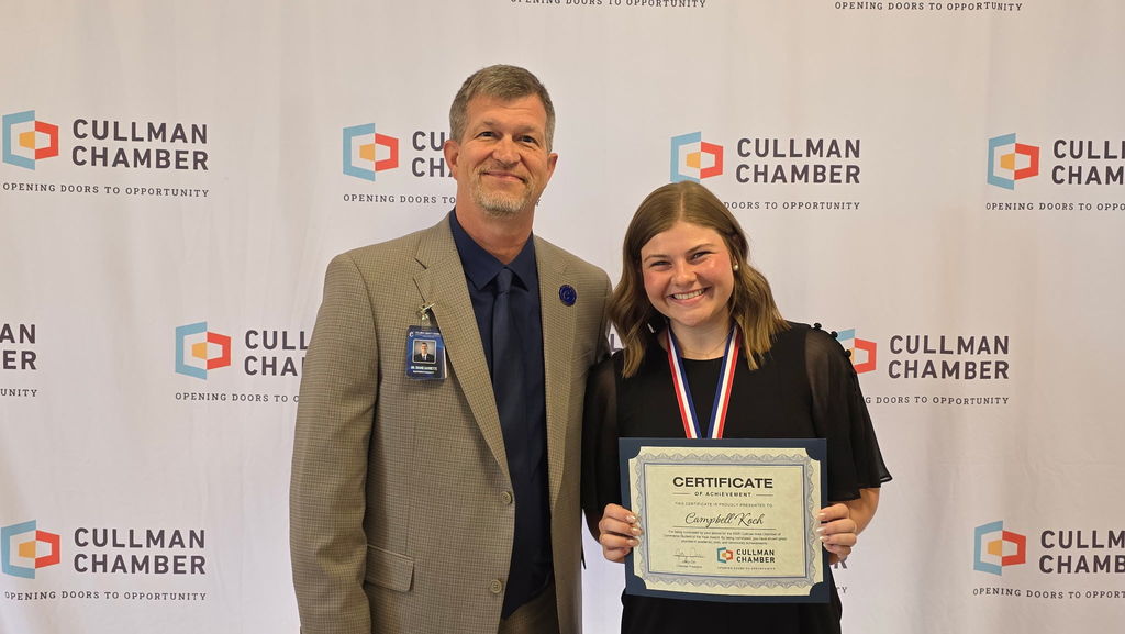 A man and woman stand next to each other in front of a Cullman Chamber banner. The woman holds a certificate.
