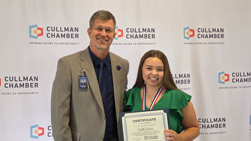 Man and woman stand behind a banner displaying the Cullman Chamber logo and name, holding a certificate.
